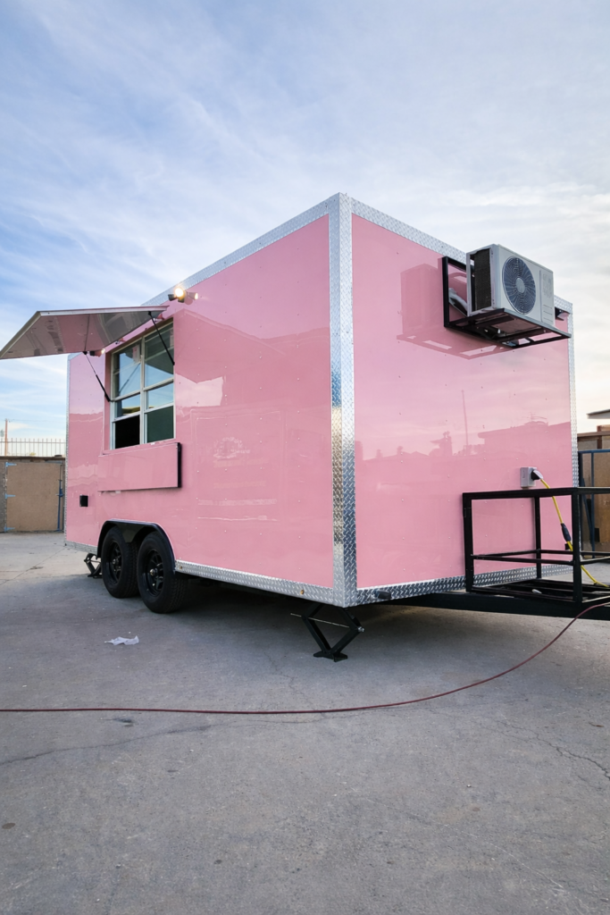 Pink custom food trailer exterior featuring an open concession serving window, diamond plate aluminum trim, heavy duty leveling jacks, and a mini-split air conditioning unit.