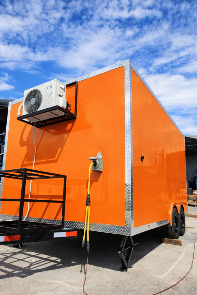 Neon Orange custom food trailer exterior detailing a mini-split air conditioner condenser and an active RV-style electrical system shore power connection.